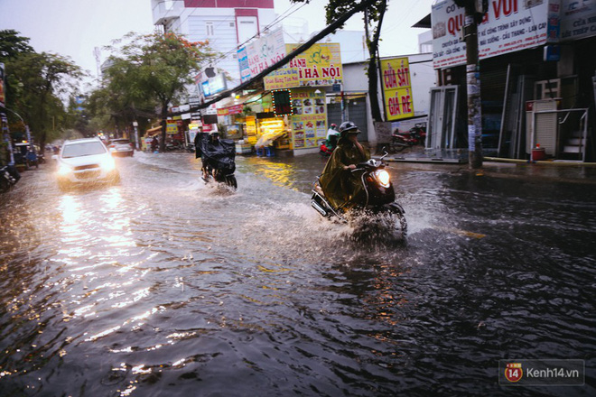 Phụ huynh ẵm bồng con nhỏ, bì bõm lội nước về nhà sau cơn mưa lớn ở Sài Gòn