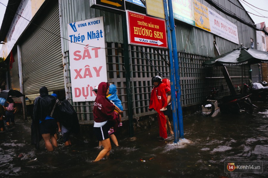 Phụ huynh ẵm bồng con nhỏ, bì bõm lội nước về nhà sau cơn mưa lớn ở Sài Gòn