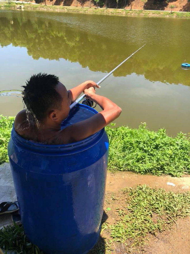 Người đàn ông ngồi hẳn trong thùng phuy vừa ngâm mình tránh nóng 40 độ, vừa thư giãn câu cá