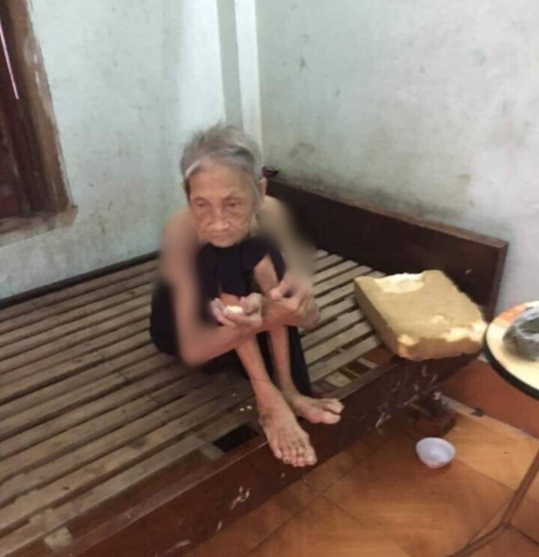 Bà Châu không mặc áo ngồi trên giường ăn bánh.