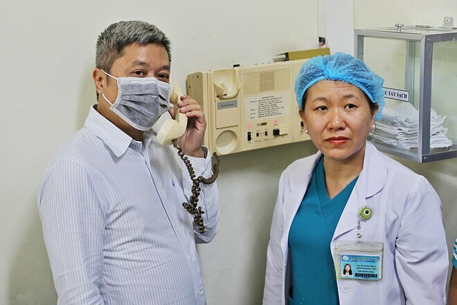 Thứ trưởng Y tế Nguyễn Trường Sơn (đeo khẩu trang) trò chuyện qua điện đàm với bệnh nhân Việt kiều nhiễm nCoV đang điều trị bên trong phòng cách ly tại Bệnh viện Bệnh Nhiệt đới ngày 9/2. Ảnh: Quỳnh Trần.