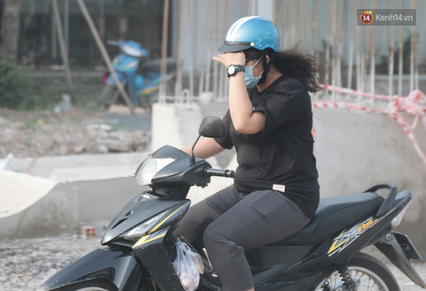 Cô gái đi xe máy dùng tay che phía trước để cản bụi bay vào mắt