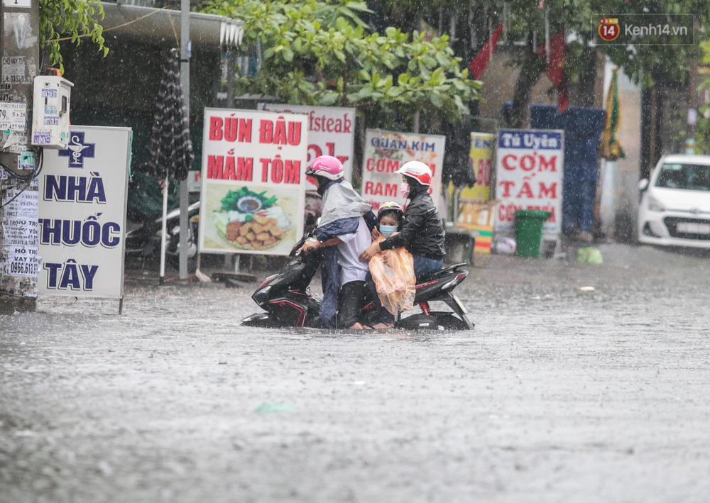 Người đàn ông chở vợ con về nhà nhưng không thể di chuyển vì đường ngập, phải tấp vào lề đường để chờ nước rút