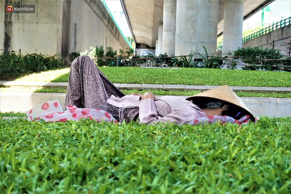 Một người phụ nữ bán vé số chọn bãi cỏ dưới gầm cầu vượt Ngã Ba Huế làm nơi ngã lưng buổi trưa