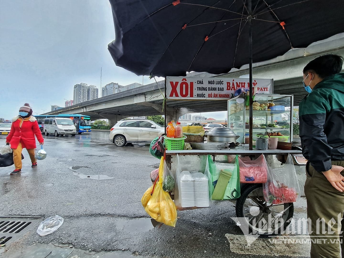 Anh Nam (quê Mỹ Đức, Hà Nội) bán hàng rong cạnh bến xe Mỹ Đình. Anh cho biết, thời tiết lạnh nên vắng khách. Vị trí anh đứng cạnh tòa nhà cao tầng nên hút gió, càng khiến cho cái rét thêm tê tái.