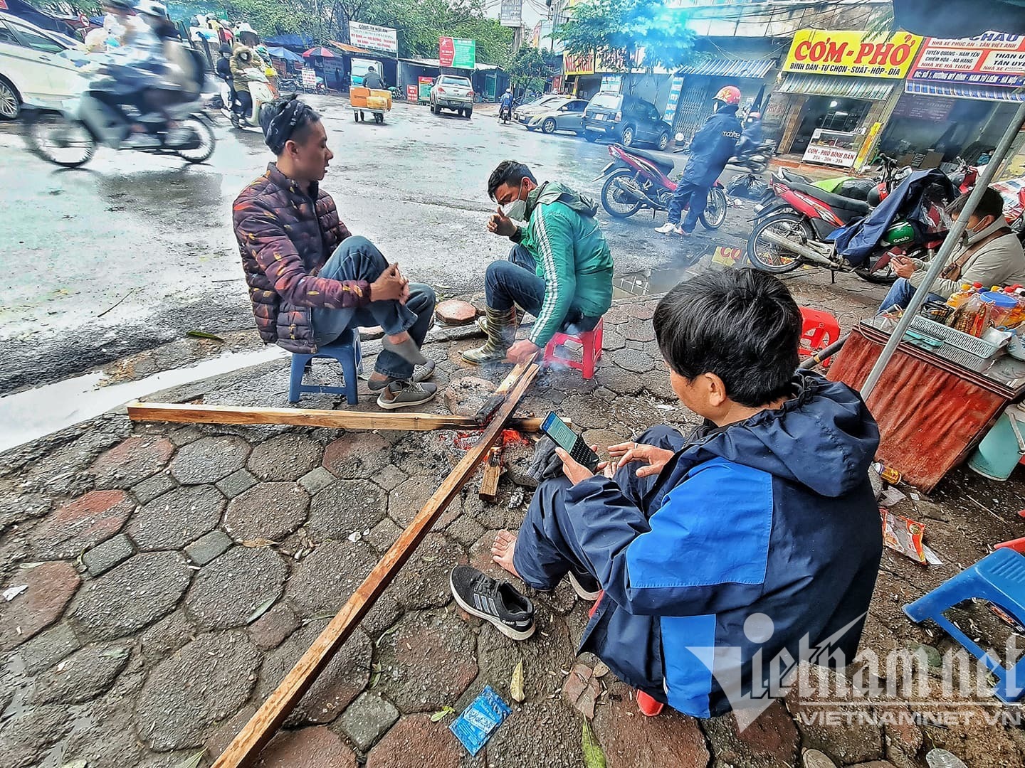 Các tài xế xe ôm ngồi sưởi ấm bên bếp củi khi chờ khách