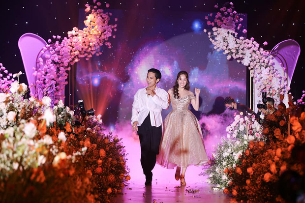 Hình ảnh của Khánh Thi và Phan Hiển diện trang phục lộng lẫy như cô dâu và chú rể với background đám cưới phía sau