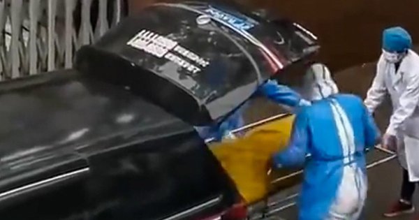 Hai người đàn ông, dường như là nhân viên nhà xác, cùng với chiếc túi đựng thi thể màu vàng bên ngoài bệnh viện phúc lợi Thượng Hải Xinchangzheng. Ảnh: SCMP