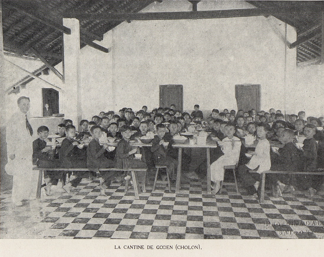 Một giáo viên đứng bên các học sinh tại nhà ăn của một trường học ở quận Gò Đen, tỉnh Chợ Lớn cũ.