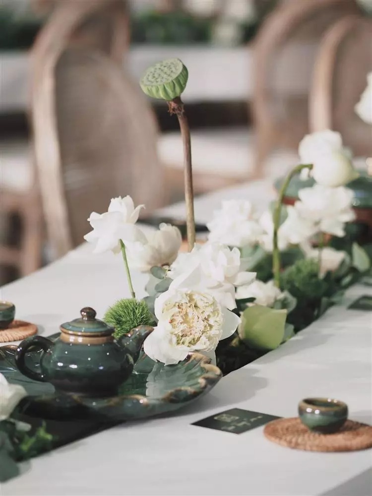 Điểm nhấn của không gian lễ ăn hỏi là bộ bàn ghế uốn lượn, được cách điệu từ hình ảnh dòng suối nhỏ thanh mát. Trên bàn, hoa sen, hoa hồng, hoa tường vi... với tông trắng được sắp xếp ở giữa bàn, tạo nên dòng suối hoa thơ mộng.