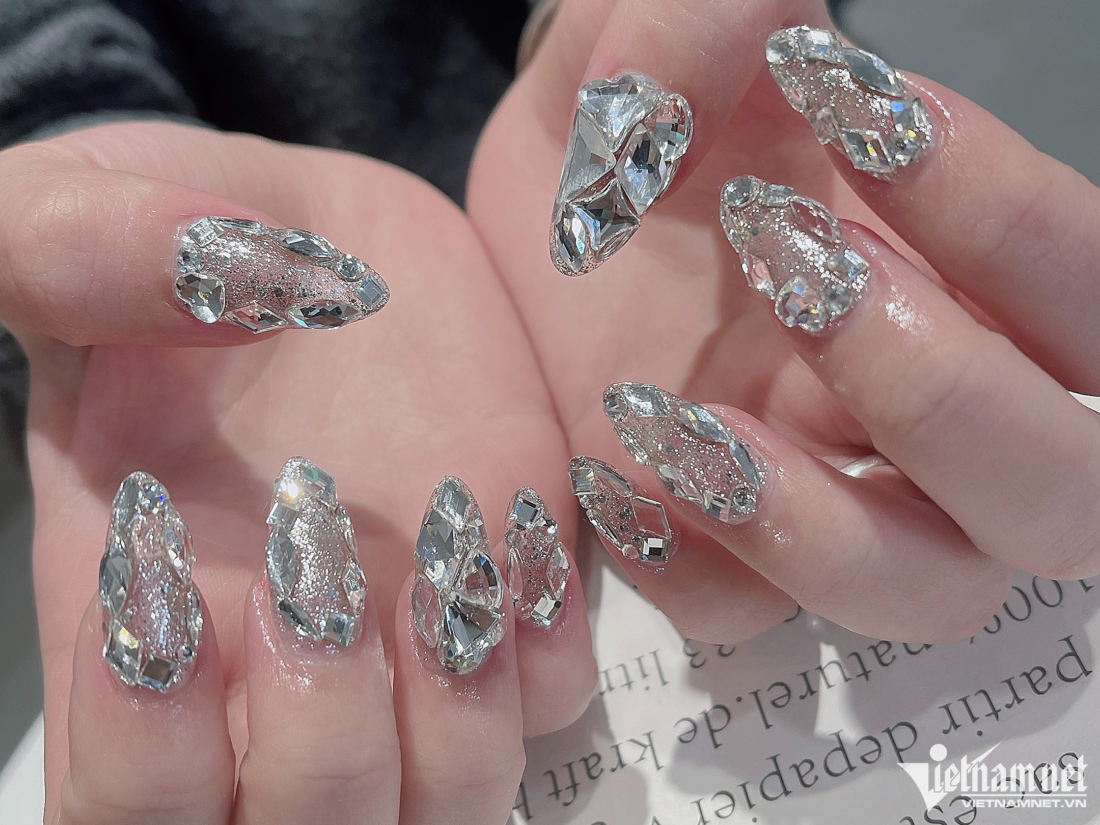 Cũng theo chia sẻ của người quản lý, một mỗi bộ sơn sửa có giá từ 210.000 đồng. Khách hàng đến thường làm úp móng và đính đá, mỗi bộ có giá từ 300.000 đến 700.000 đồng. Nếu sử dụng thêm dịch vụ trang trí bằng nhiều loại phụ kiện, giá mỗi bộ có thể lên đến 3 triệu đồng. Trong hình là bộ móng mà chị Cải mới làm xong cho khách có giá 2,5 triệu.