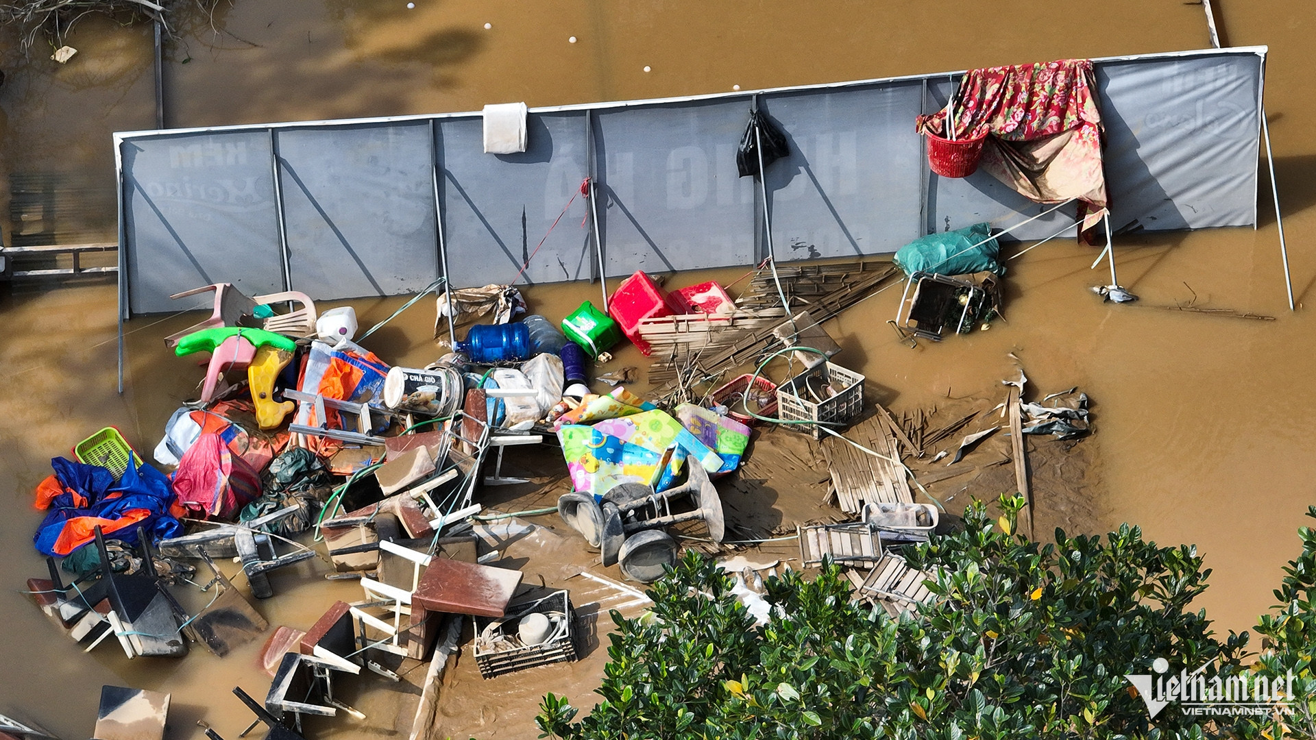Nhiều đồ dùng bị nước đánh xô dạt vào một góc trước biển quảng cáo.