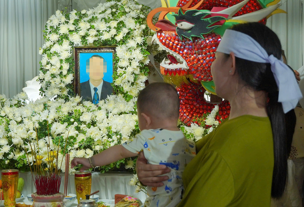 Chị Ngân ôm con thơ nhìn về di ảnh của chồng. Ảnh: H.T