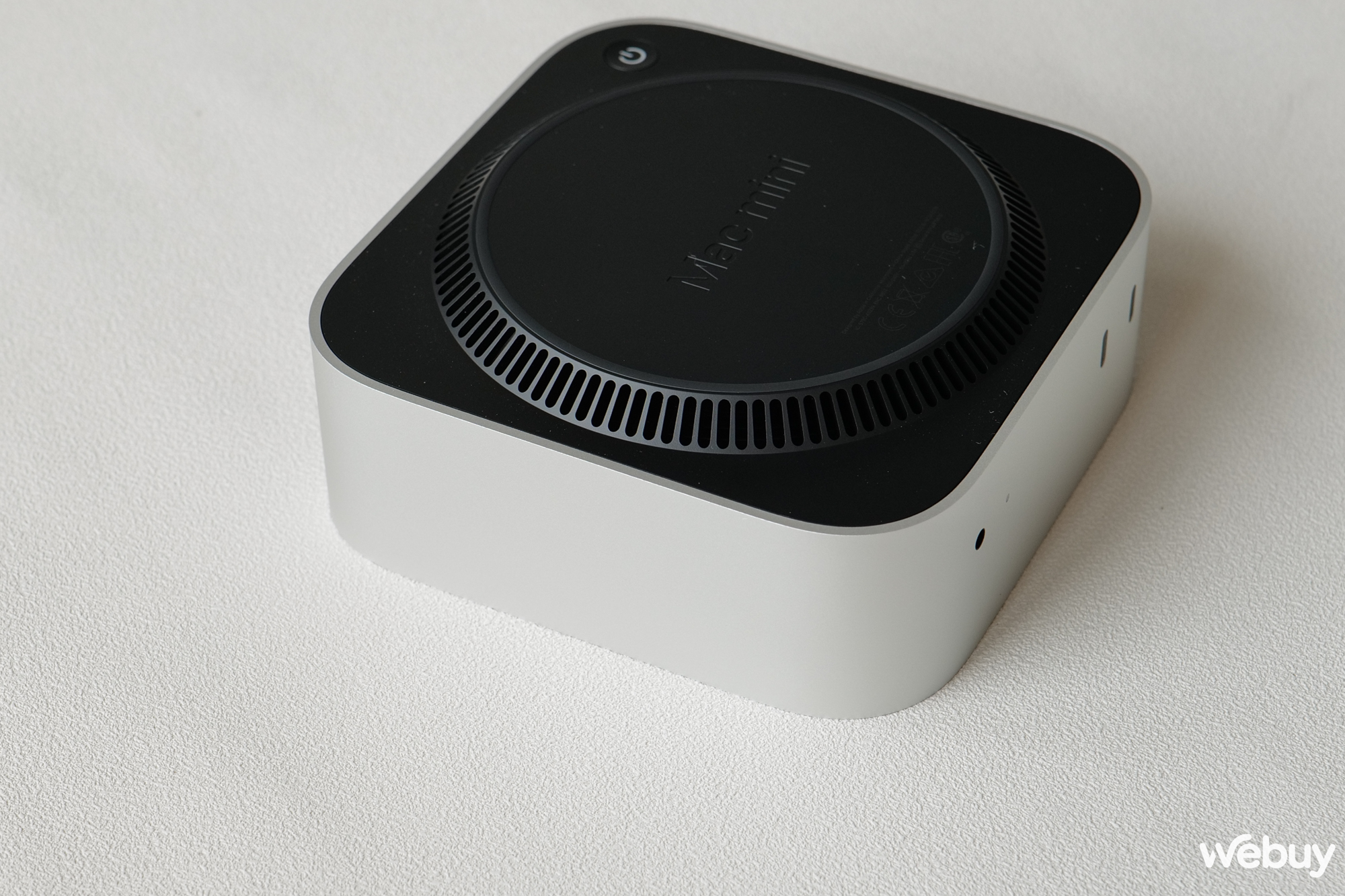 Có một khoảng nâng lên từ dưới đáy đến phần cạnh chứa nút nguồn. Nơi đây ta có thể thấy các khe tản nhiệt. Mac mini cũng tích hợp loa trong trường hợp bạn kết nối với màn hình không có loa hoặc không sử dụng loa ngoài.