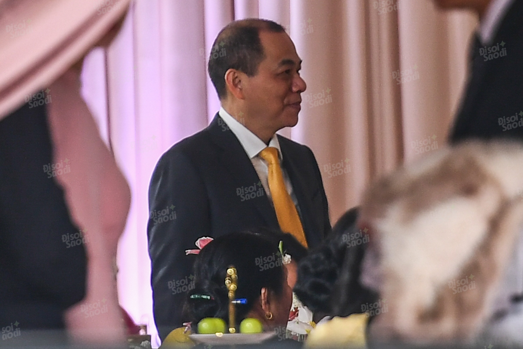 Vị tỷ phú diện áo vest đen cùng cà vạt màu vàng, mỉm cười suốt buổi lễ.