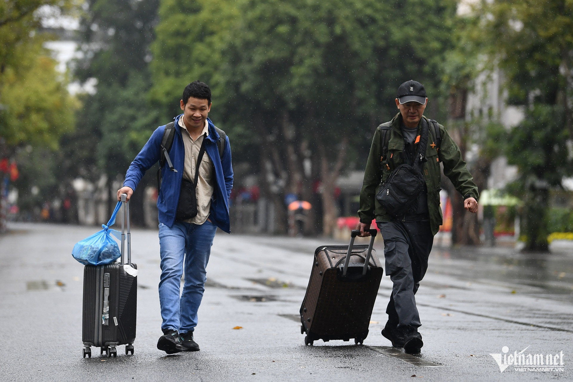 Hai du khách người Trung Quốc kéo vali từ khách sạn qua phố đi bộ trong mưa để ra khu vực ô tô đỗ phía phố Hai Bà Trưng.