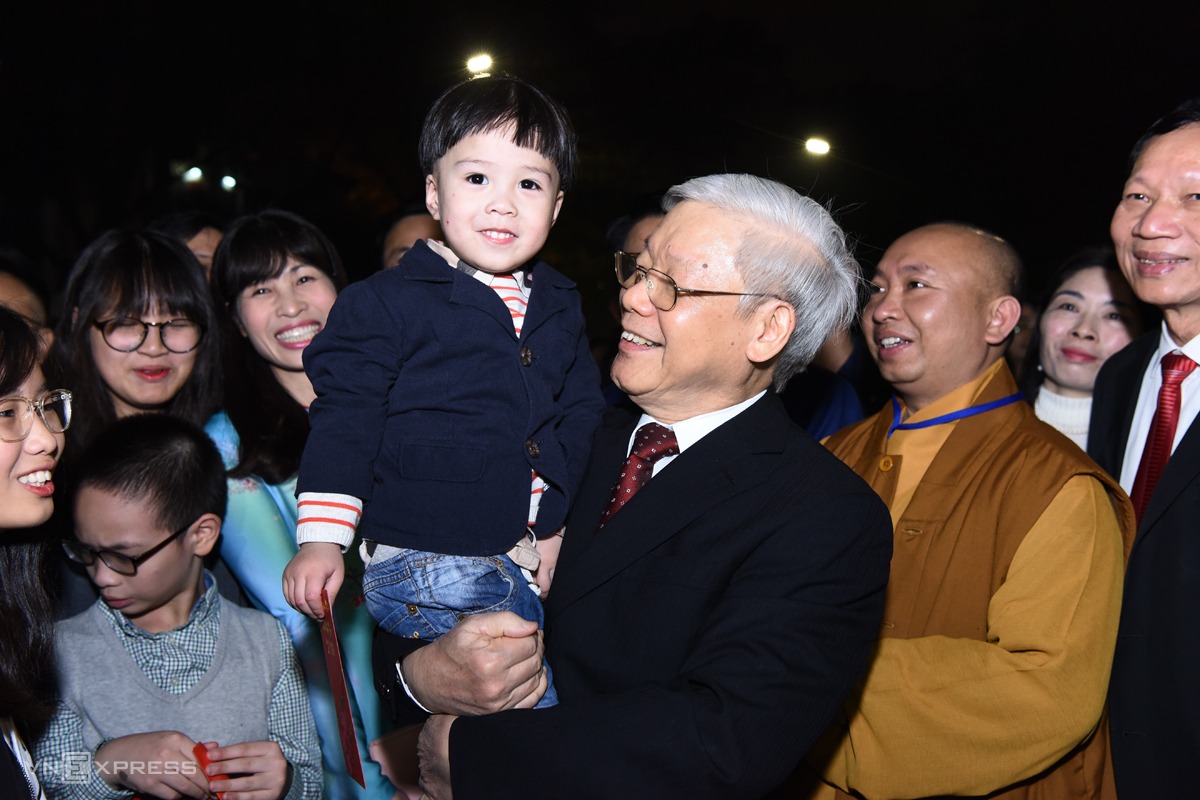 Đêm 30 Tết Mậu Tuất 2018, Tổng bí thư Nguyễn Phú Trọng đến phố đi bộ Hồ Gươm, Hà Nội, trò chuyện với người dân đang chờ đón giao thừa trước tượng đài Lý Thái Tổ. Ông chúc Tết công nhân môi trường đô thị đang làm nhiệm vụ, mừng tuổi các cháu bé đang cùng gia đình tề tựu quanh Hồ Gươm. Khi một cháu nhỏ lại gần, Tổng bí thư cười tươi, bế bổng cháu bé để cùng chụp hình lưu niệm. Ảnh: Giang Huy