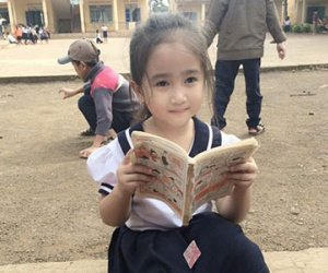 Cô bé tiểu học ở Đắc Lắk gây sốt với bức ảnh ngồi đọc truyện ở sân trường
