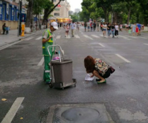 Cô gái trẻ cúi xuống hót phân chó trên đường cho vào thùng rác