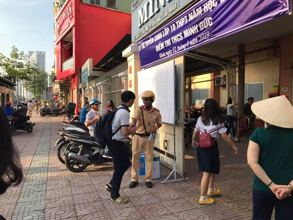 Hai chiến sỹ CSGT đứng trước cổng trường phát nước miễn phí cho thí sinh và phụ huynh ở Sài Gòn