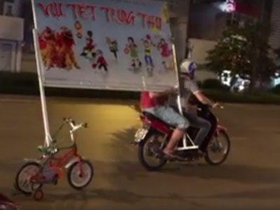 Hai nam thanh niên tận dụng xe đạp trẻ em để vận chuyển biển hiệu trên đường phố Hà Nội