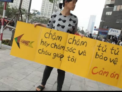 Phụ nữ Hàn Quốc cầm biển chặn dòng xe leo lên vỉa hè ở Hà Nội