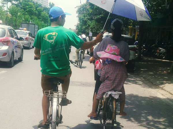 Hình ảnh dễ thương ngày Hà Nội nóng đỉnh điểm: Người đàn ông chạy xe đạp che ô cho hai mẹ con trên phố